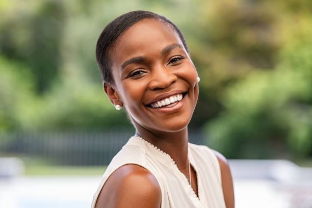 Portrait of smiling middle aged african woman looking at camera. Cheerful black mid adult woman smiling outdoor. Close up face of beautiful black lady laughing at park.